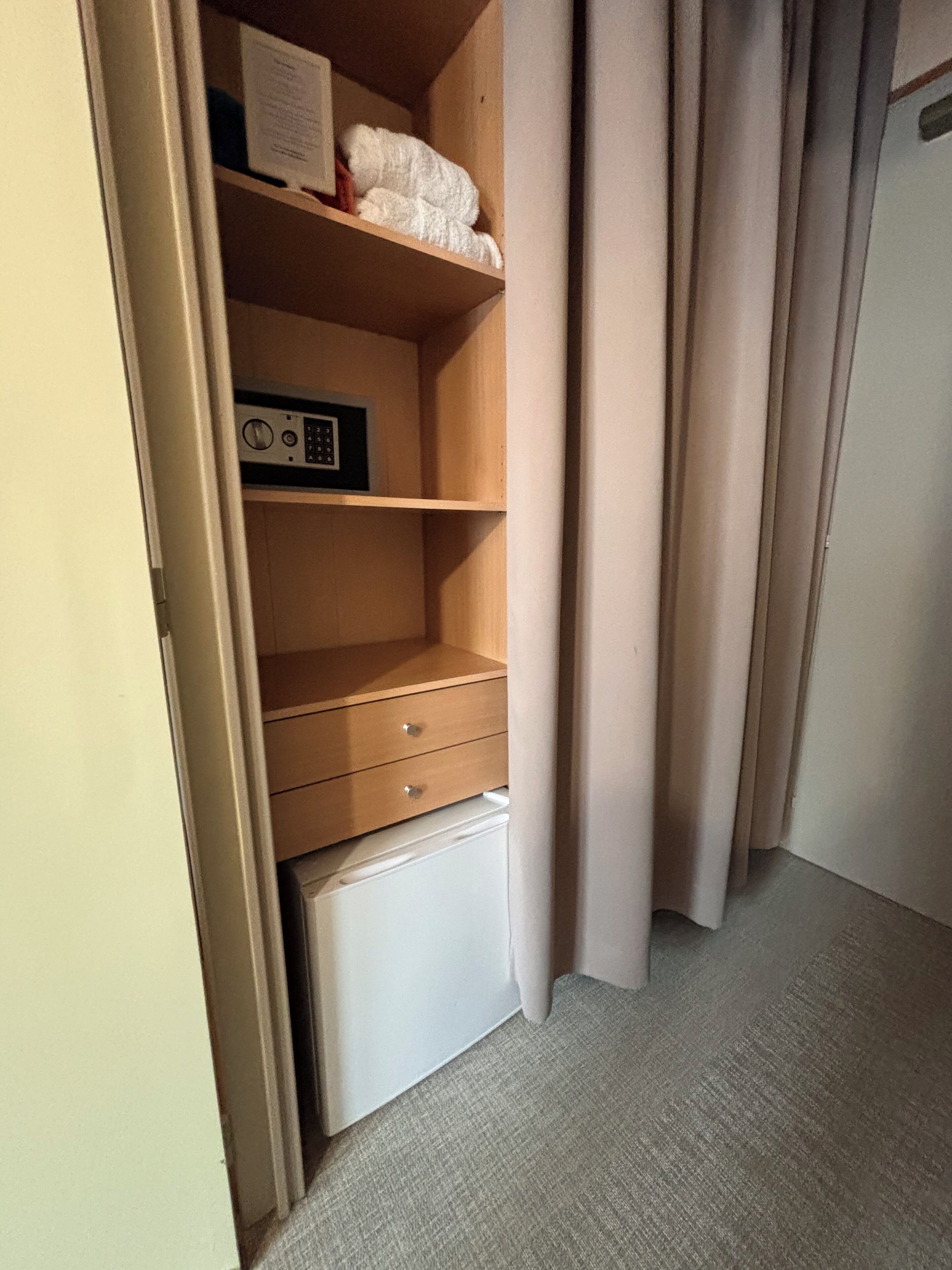 A room with a wooden wardrobe, a small white appliance, and a curtain.