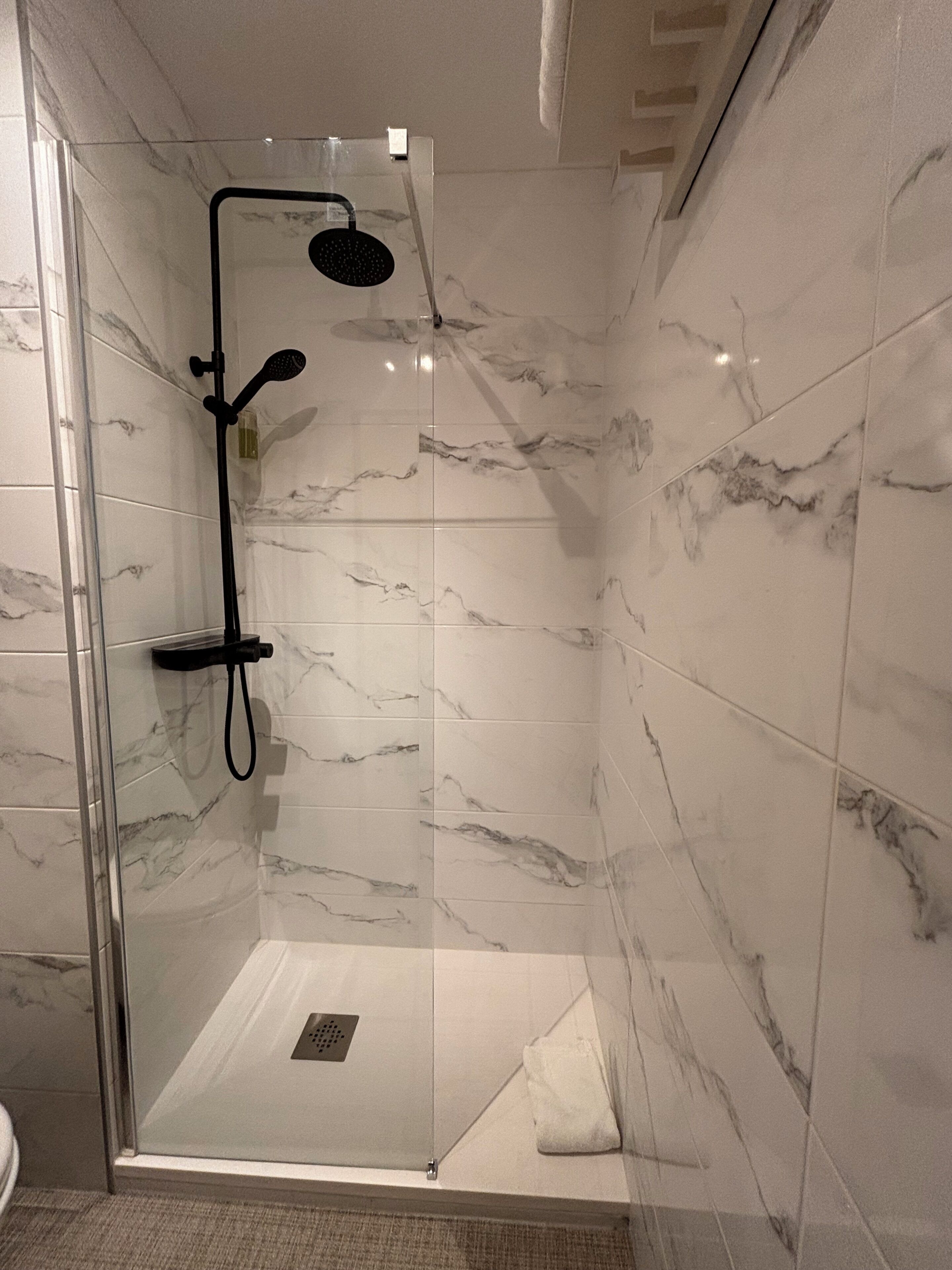 A glass-enclosed shower with a handheld showerhead and a wall-mounted control panel.