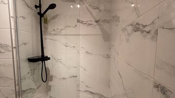 A glass-enclosed shower with a handheld showerhead and a wall-mounted control panel.