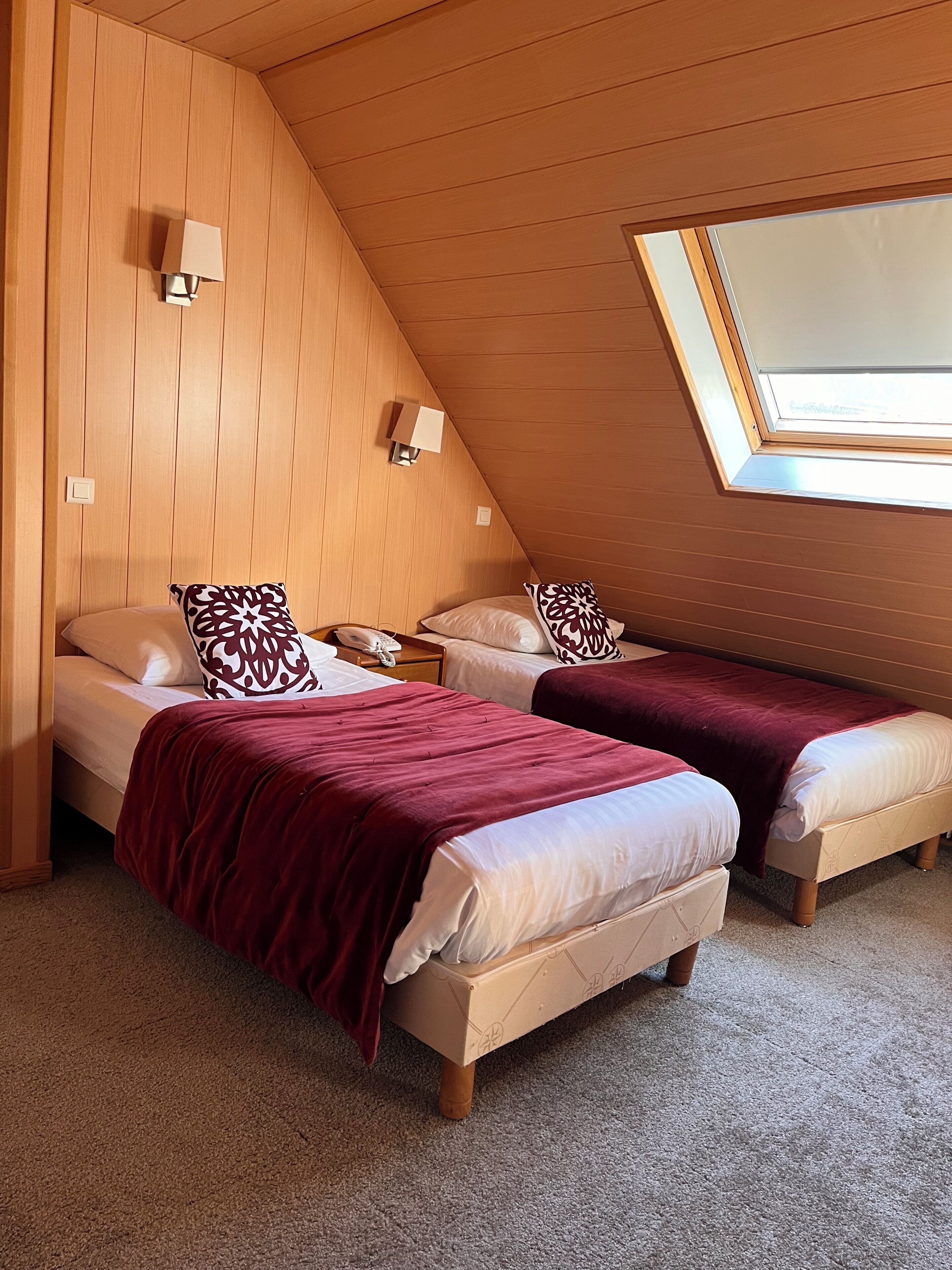 Ein Zimmer mit zwei Betten, einem schrägen Holzbalken und einem Oberlicht.