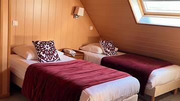 Ein Zimmer mit zwei Betten, einem schrägen Holzbalken und einem Oberlicht.