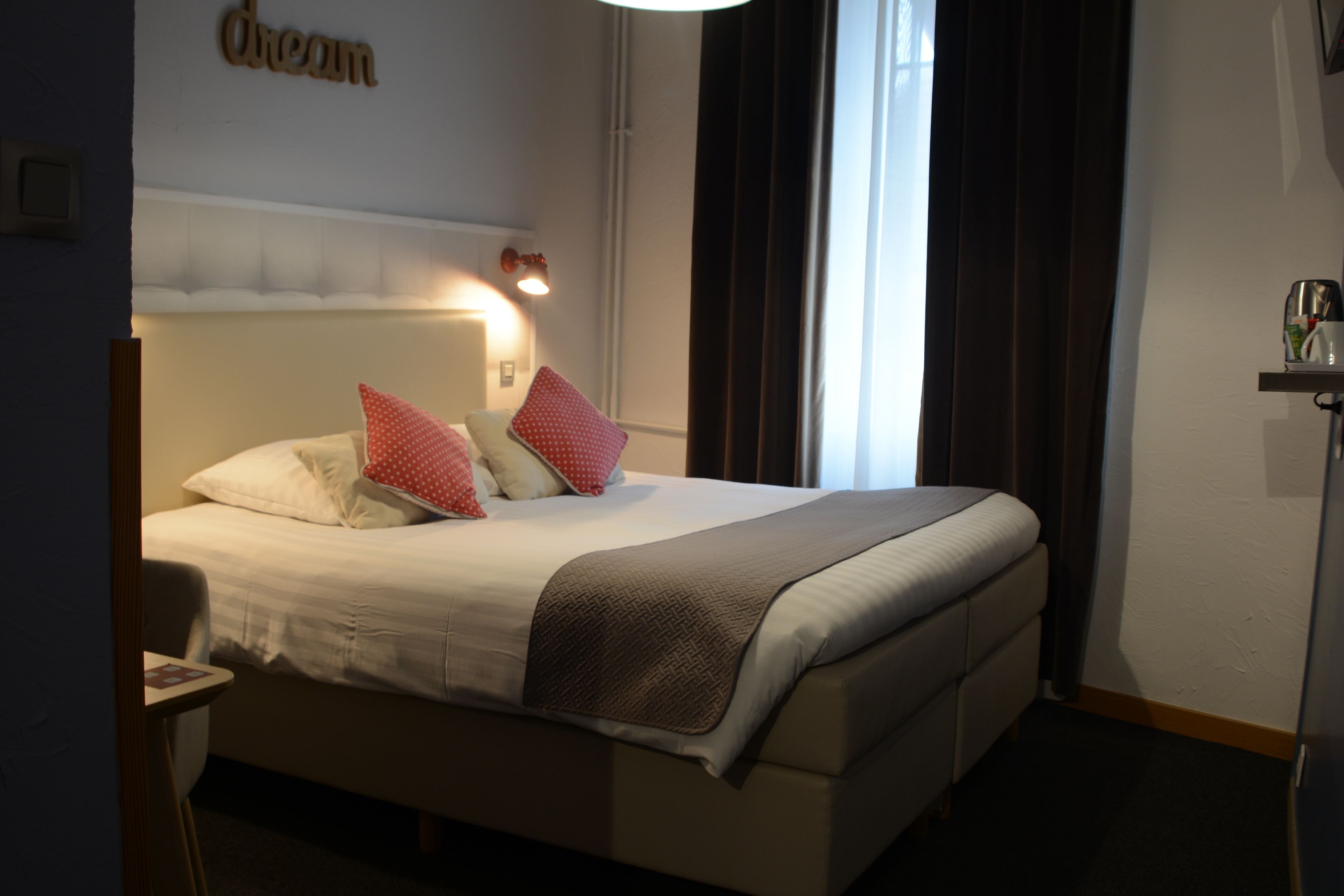 A hotel room with a bed, pillows, a bedside lamp, and a nightstand.