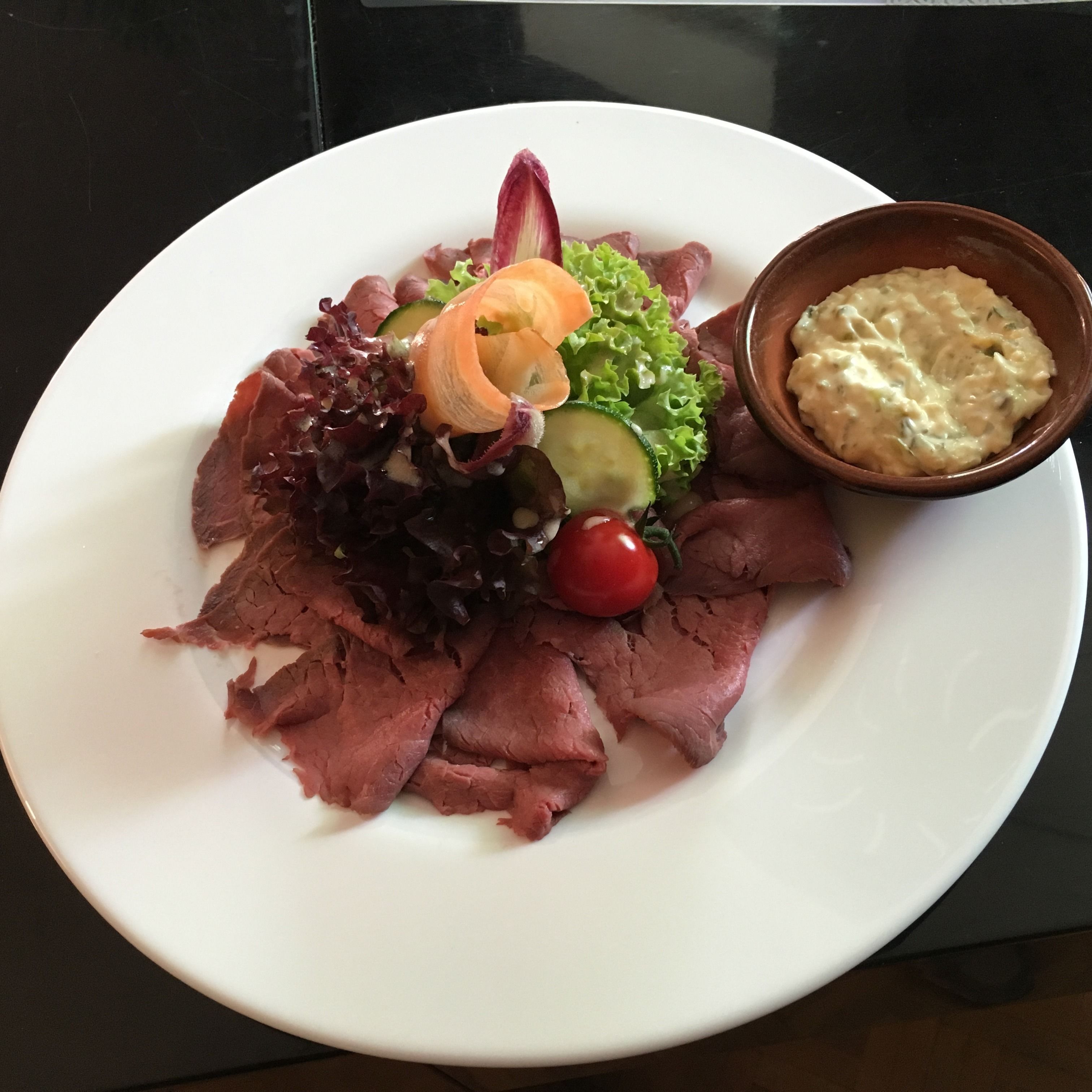 A plate of sliced meat, vegetables, and a bowl of dip.