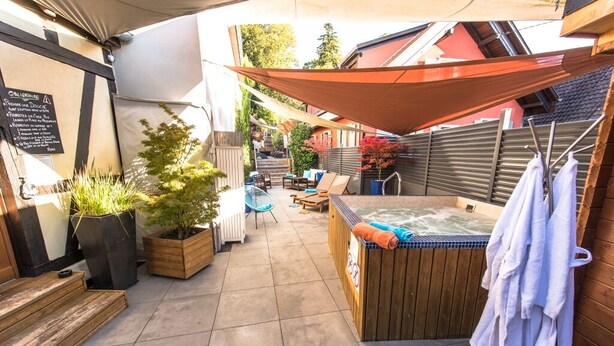 A cozy outdoor patio area with a hot tub, seating, and a wooden deck. - Au Cheval Blanc Hôtel et Restaurant (Ribeauvillé)