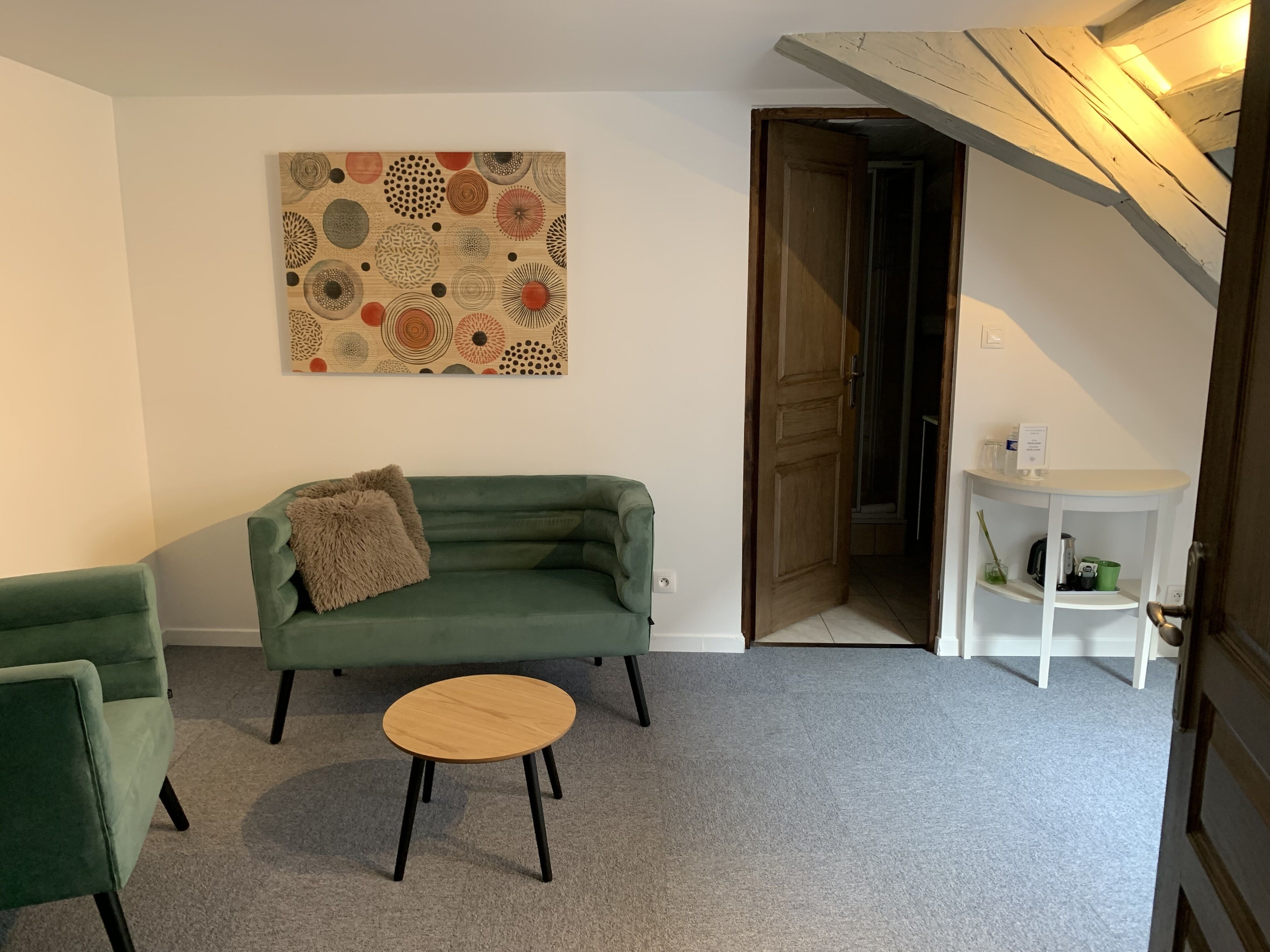 A room with a green sofa, a round wooden table, and a wall-mounted abstract art piece.