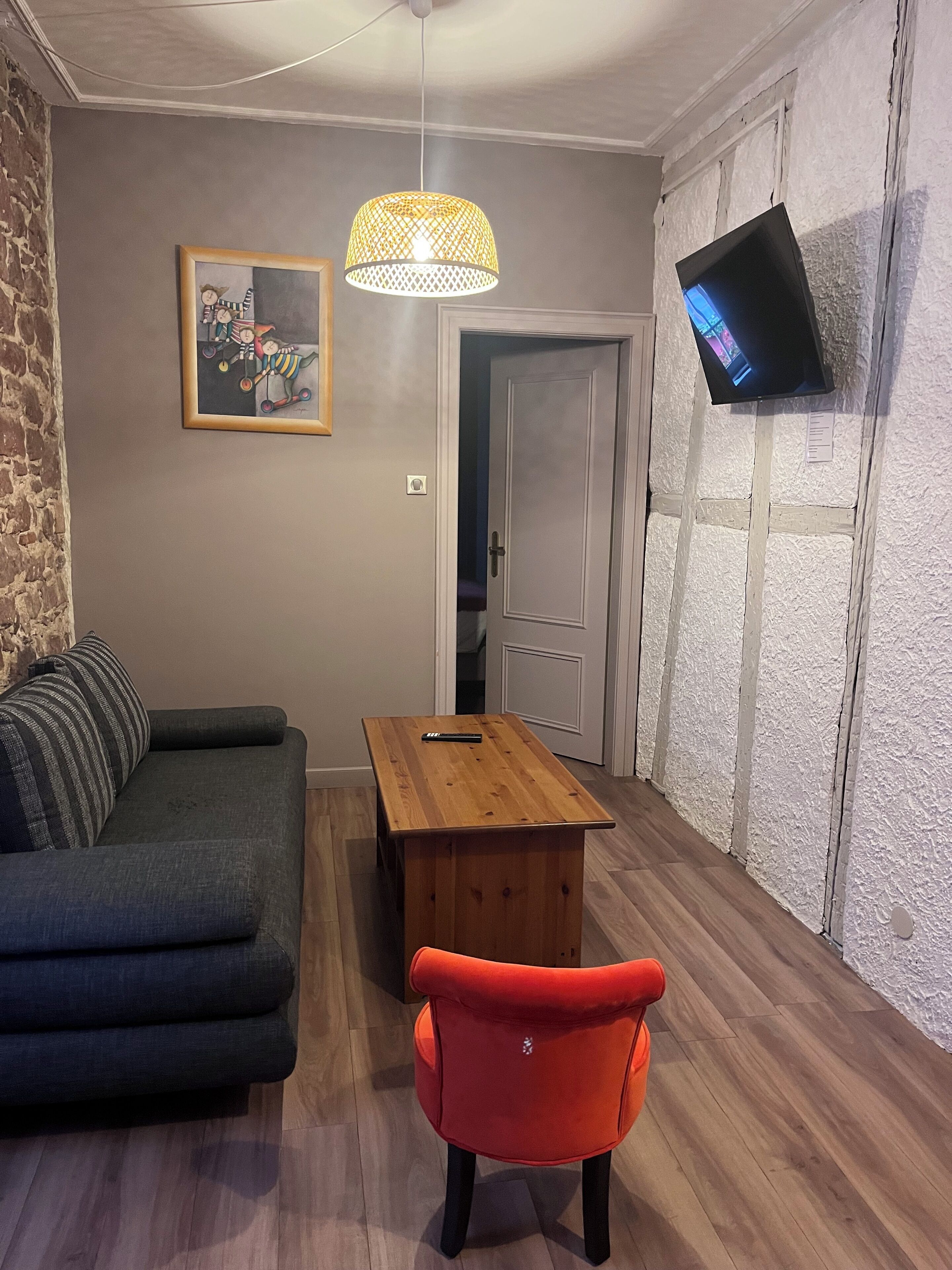 A living room with a sofa, a wooden coffee table, a red chair, a hanging lamp, and a TV mounted on the wall.