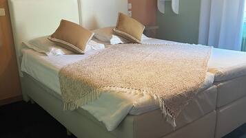 A neatly made bed with a patterned blanket and two pillows, a wall-mounted light fixture, and a mirror with a shelf above it.