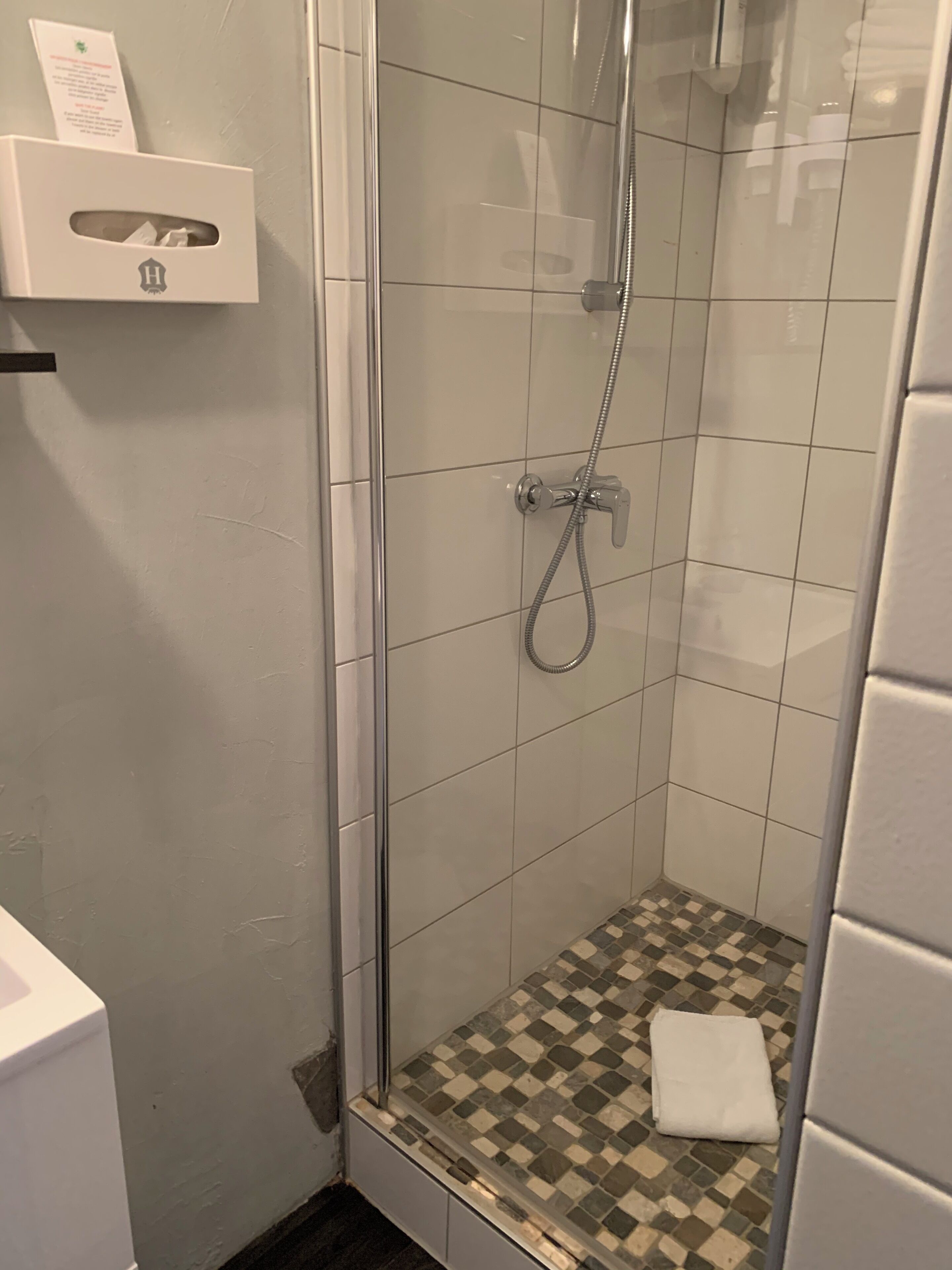 Una ducha con puerta de cristal, piso de baldosas y una toalla en el suelo.