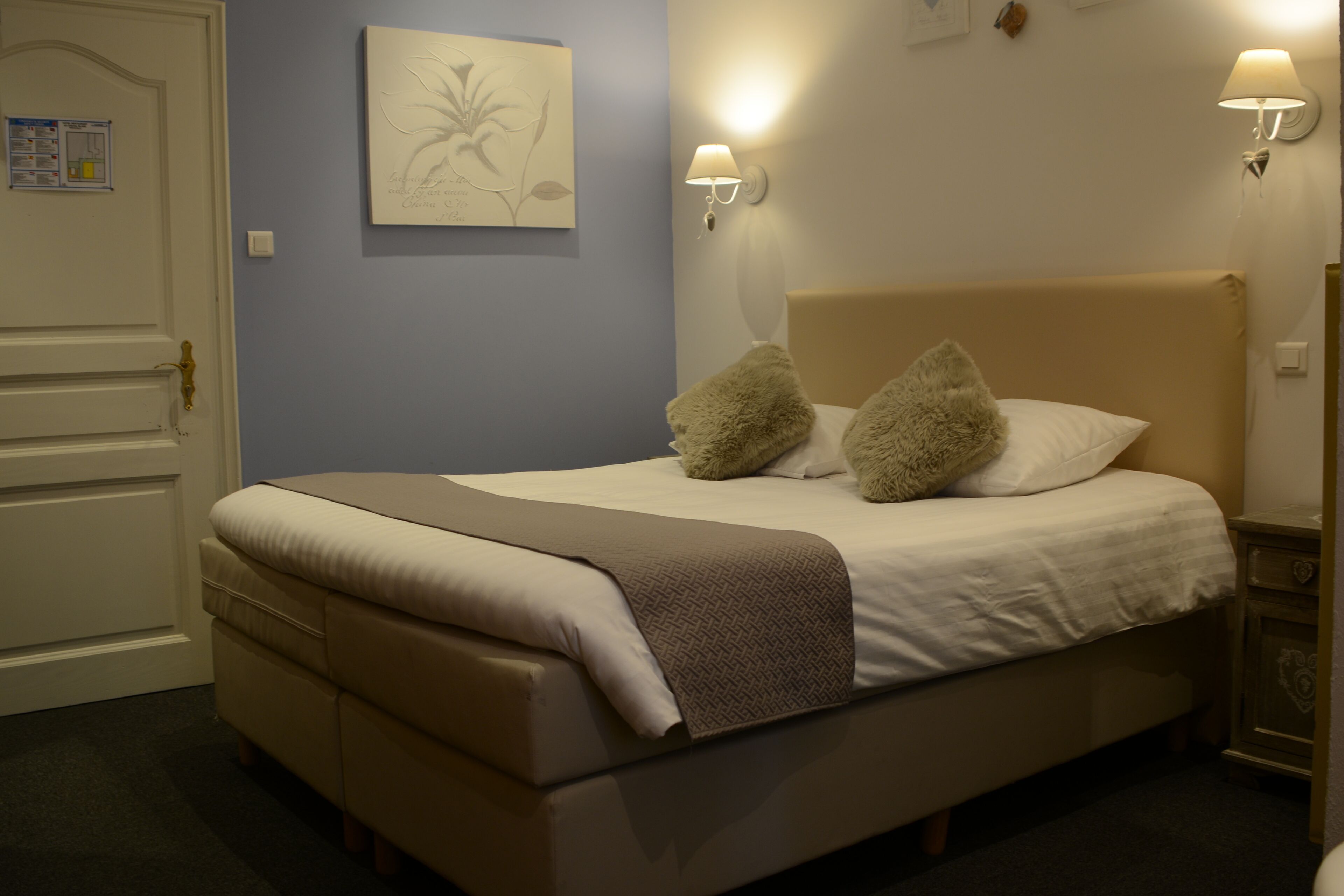 A bed with a headboard, two pillows, a blanket, and two wall-mounted lamps.