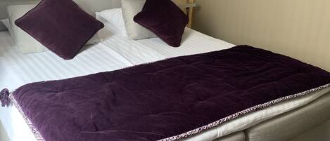 A bed with a headboard, two pillows, a blanket, a wall-mounted phone, and a painting.