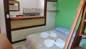 A small, compact room with a bed, a wooden desk, and a mirror. - Rota de Geribá Suítes (Búzios)