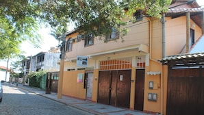 A building with a yellow facade, a gated entrance, and a cobblestone street. - Rota de Geribá Suítes (Búzios)