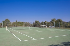 A tennis court with a net, surrounded by trees and a fence.