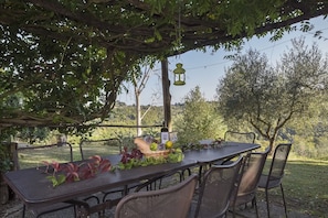 An outdoor dining area with a table and chairs under a pergola, surrounded by greenery and trees. - Bosco Lazzeroni Residence (Montaione)