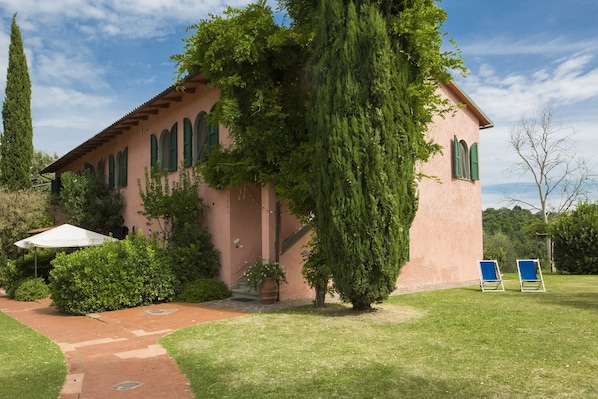 A pink building with arched windows and a pathway leading to a white umbrella.