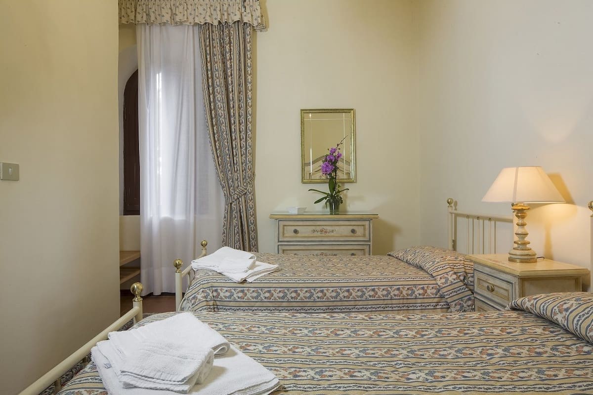 A hotel room with a bed, a bedside table with a lamp, a dresser, and a mirror.