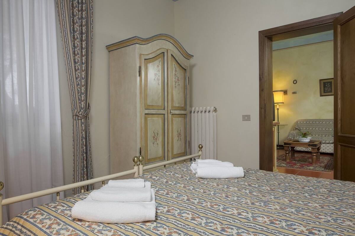 A bedroom with a bed, a wardrobe, a radiator, a door leading to another room, and a lamp.