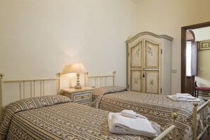 A hotel room with two beds, a nightstand with a lamp, a wardrobe, and a mirror.