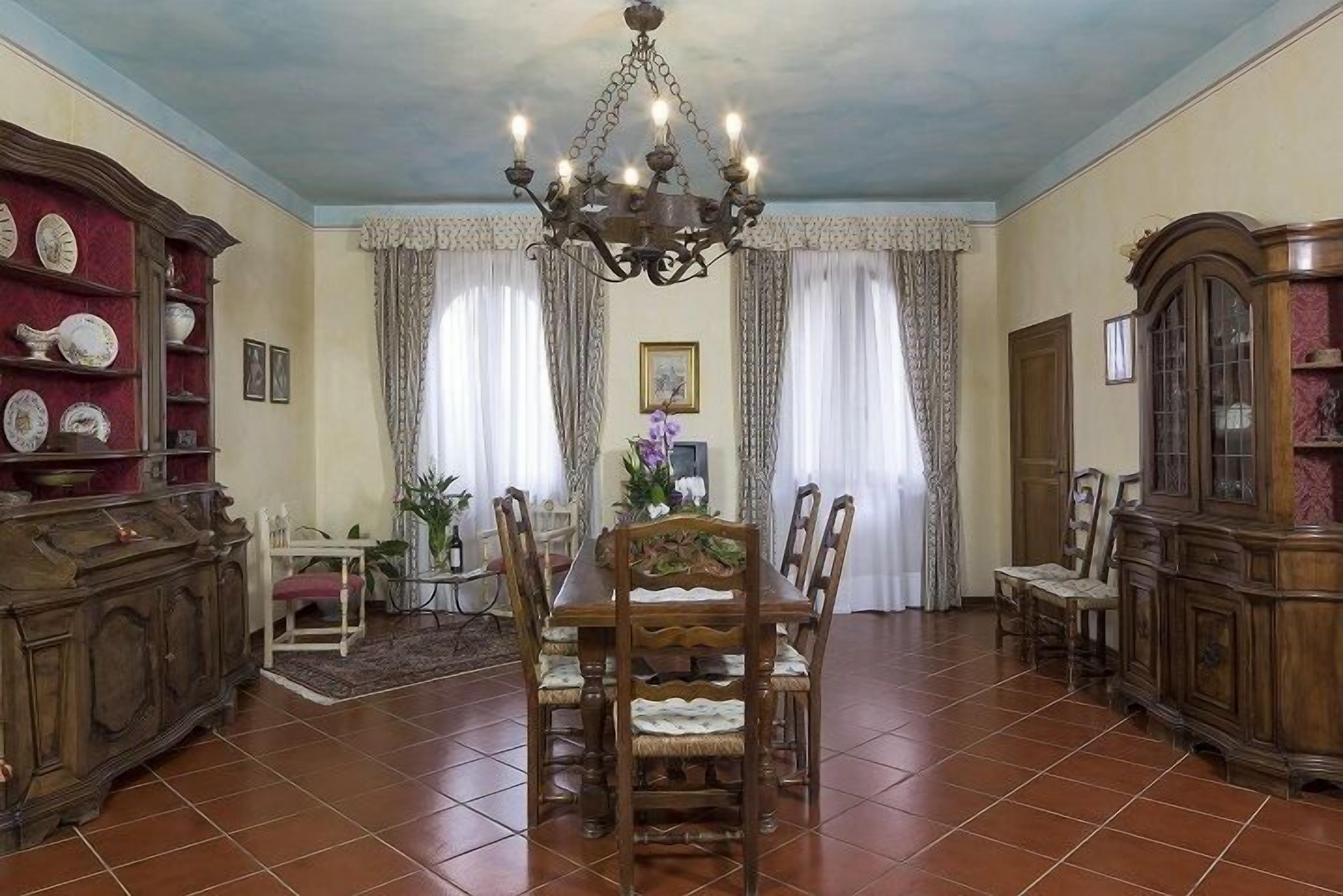 A dining area with a wooden table and chairs, a chandelier, and a cabinet with plates.