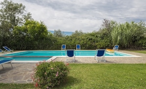 A rectangular swimming pool with a stone deck, surrounded by blue lounge chairs.