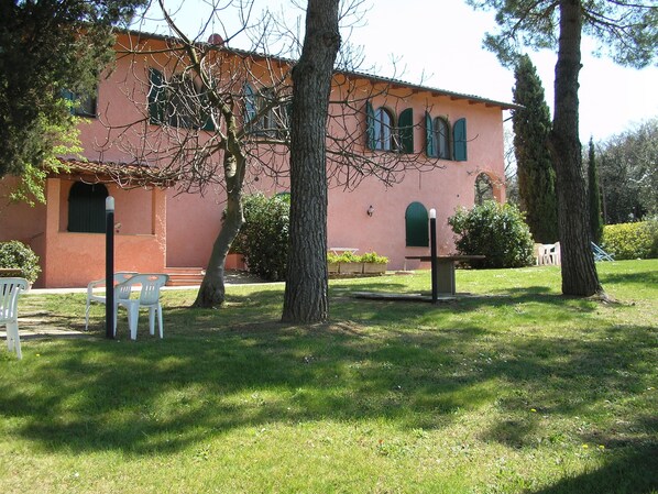 A building with a pink facade, arched windows, and a small garden area with chairs and trees. - Bosco Lazzeroni Residence (Montaione)