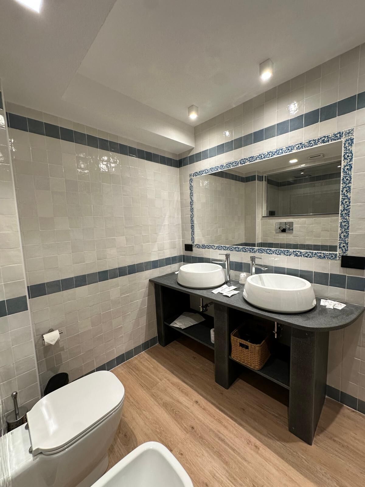 A modern bathroom with two sinks, a toilet, and a large mirror.