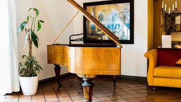 A grand piano in a room with a tiled floor, a potted plant, a framed painting, and a yellow sofa.
