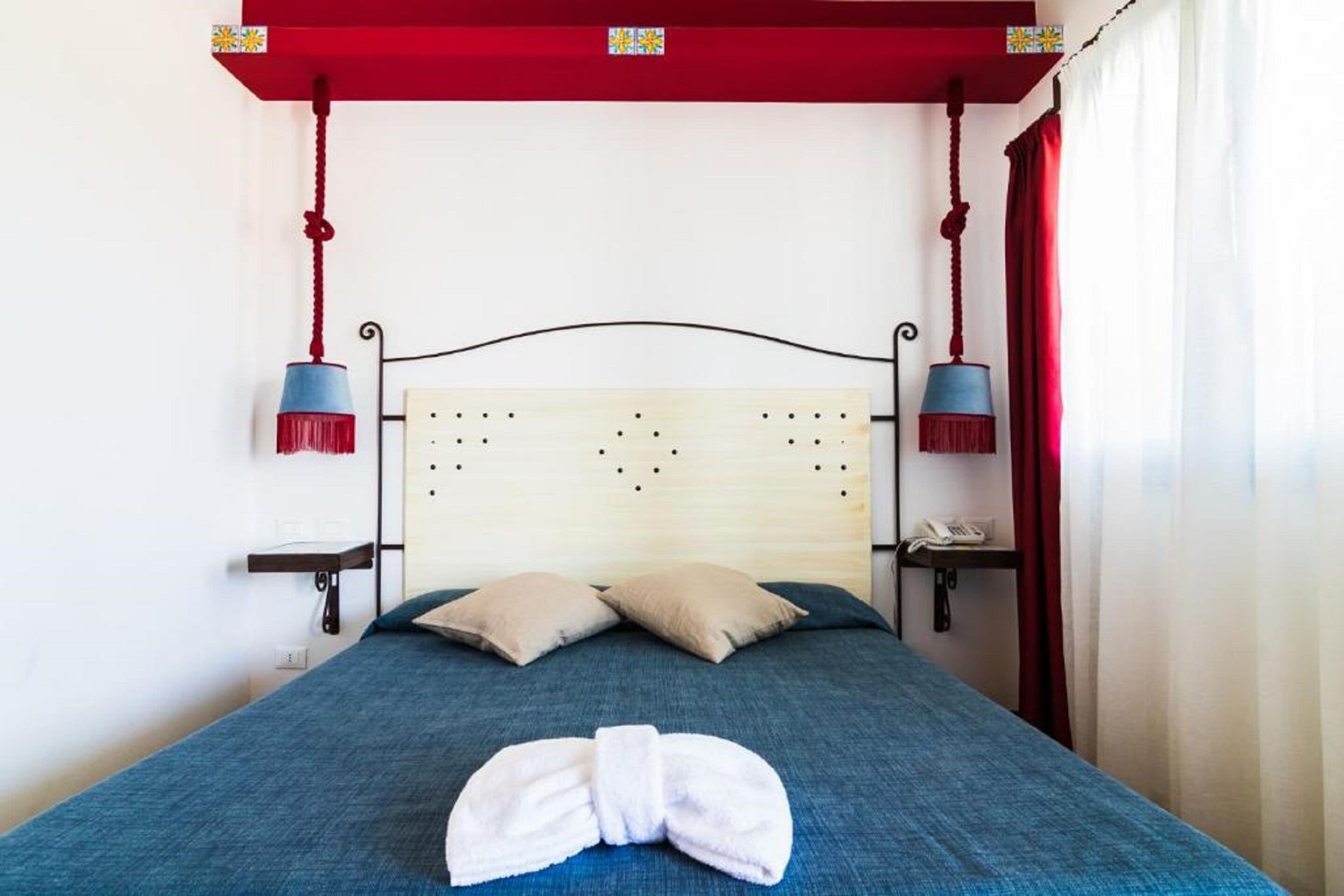 Ein Hotelzimmer mit einem Bett, zwei Kissen, einem Handtuch, einem Nachttisch mit Telefon und einem roten Baldachin.