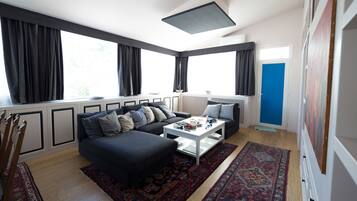 Een moderne woonkamer met een hoekbank, een salontafel en een groot raam met gordijnen.