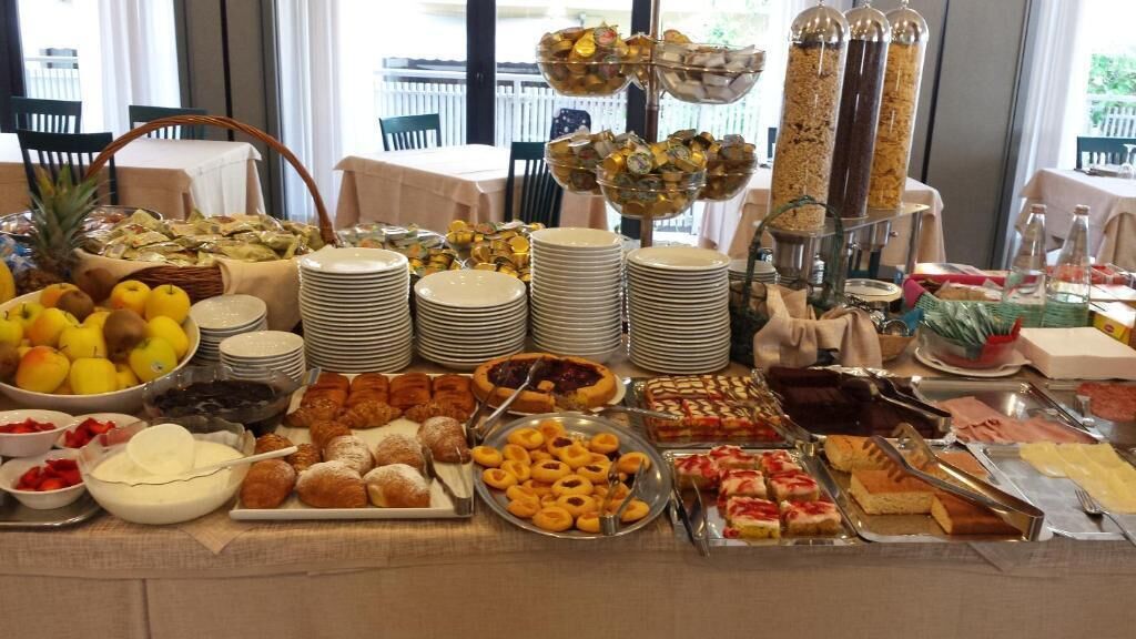 Una mesa de buffet con diversos alimentos, entre ellos frutas, pasteles y postres, dispuestos en platos y fuentes.