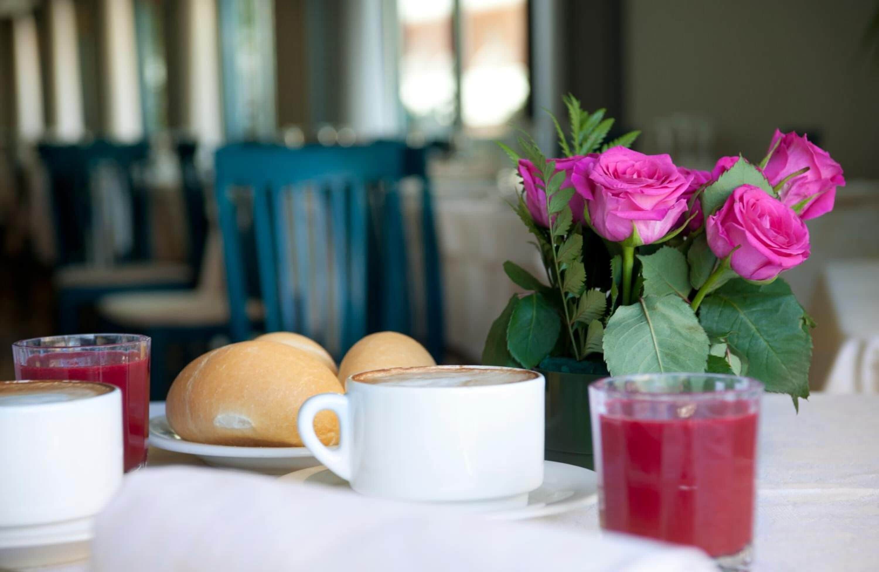 A breakfast setting with pastries, a cup of coffee, and a vase of pink roses.