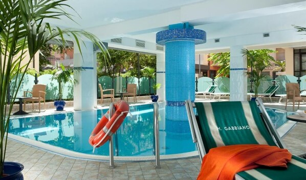 An indoor swimming pool with lounge chairs, a lifebuoy, and a blue-tiled column.