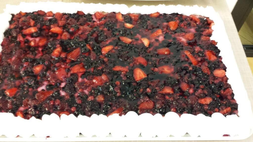 Un plat rectangulaire pour desserts, bordé de blanc, rempli d’une compote de fruits rouges et garni de fraises entières.