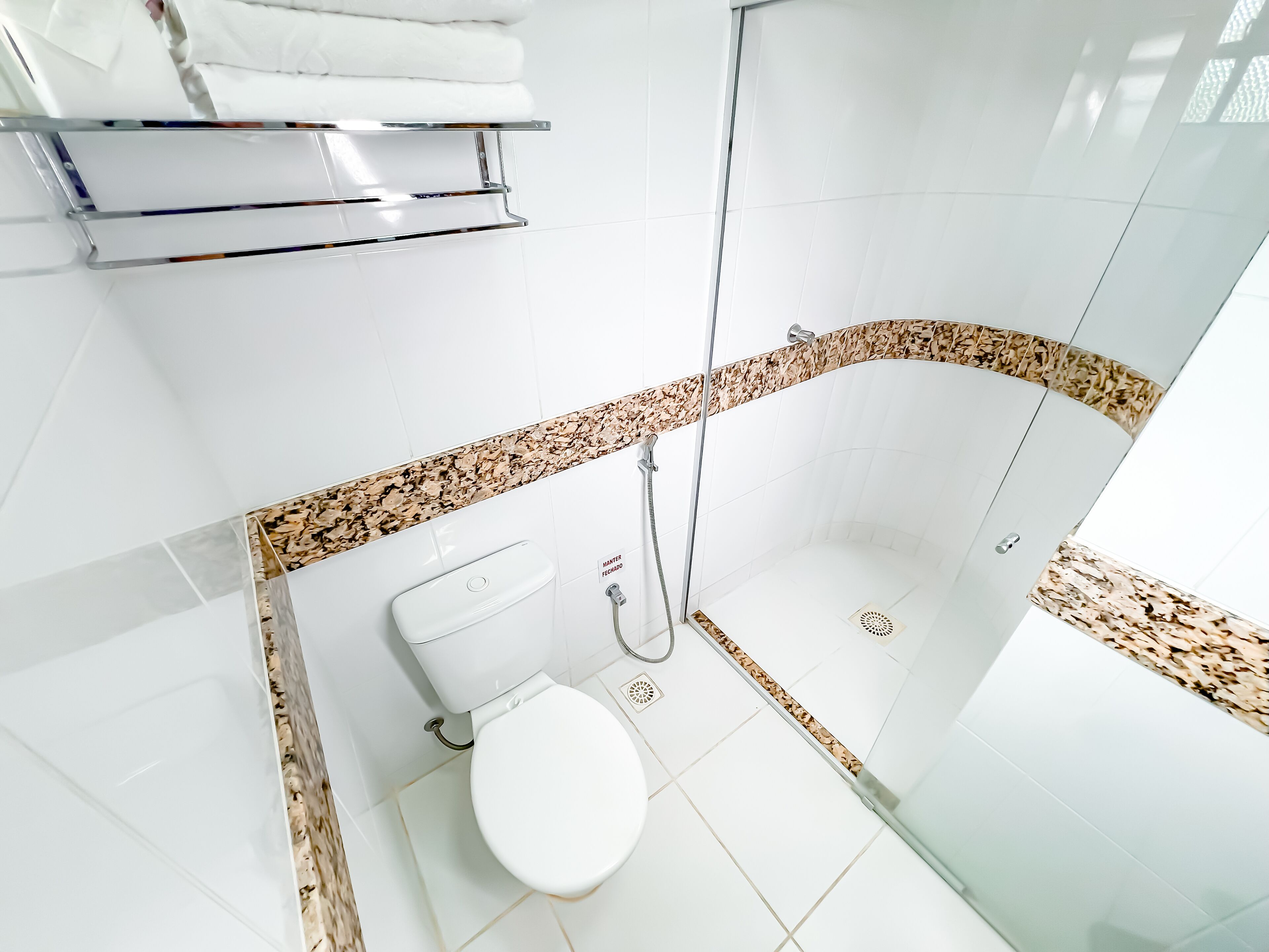 A modern bathroom with a white toilet, a glass shower enclosure, and a marble-tiled shower area.
