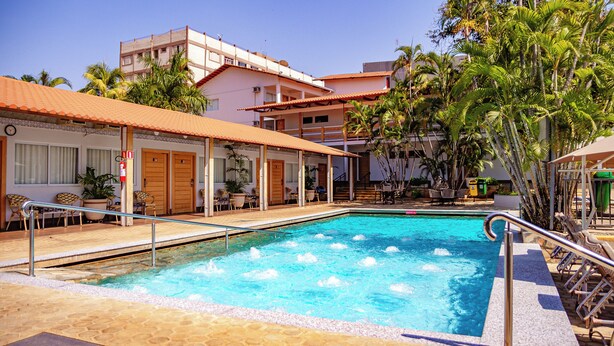 A swimming pool with a tiled deck, surrounded by lounge chairs and a building with multiple balconies. - Hotel Roma - Direto com o Grupo DiRoma - acesso ao Acqua Park com café da manhã (Caldas Novas)