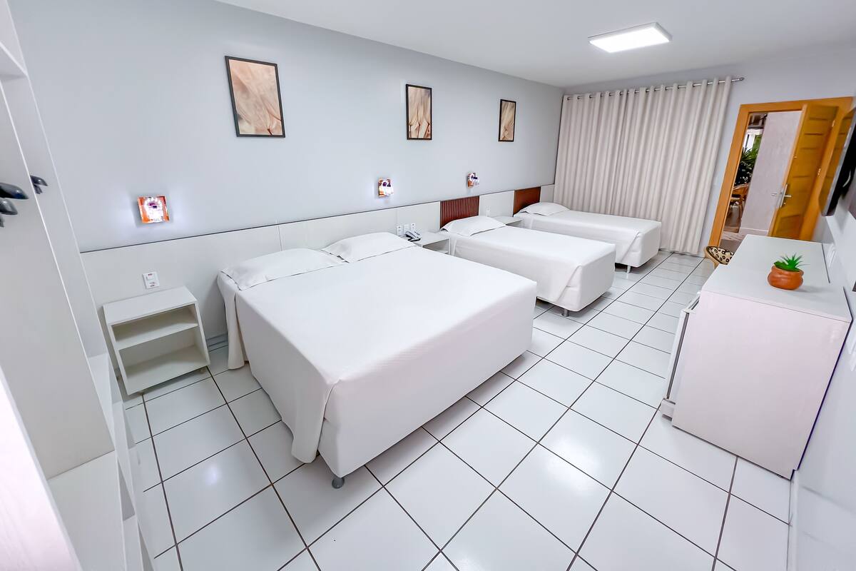 A hotel room with three single beds, a small desk, a nightstand, and a potted plant.