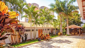 A courtyard with a stone floor, palm trees, a wooden bench, and a small garden area. - Hotel Roma - Direto com o Grupo DiRoma - acesso ao Acqua Park com café da manhã (Caldas Novas)