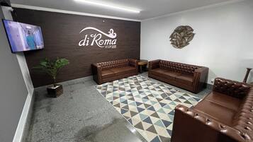 Um hall com um sofá de couro marrom, um tapete estampado, uma televisão na parede e um ornamento decorativo.