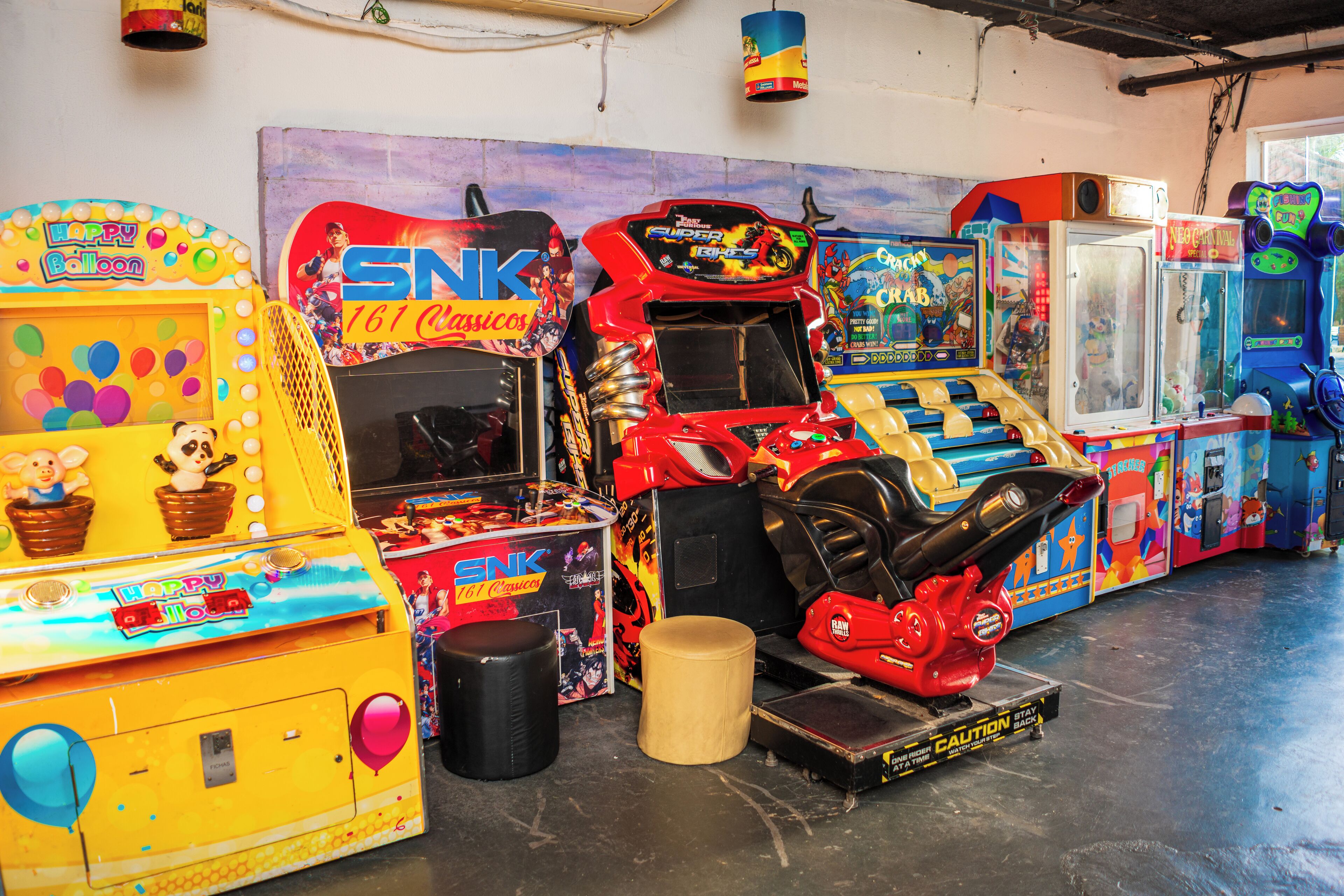 Een rij spelautomaten in een ruimte met een betonnen vloer en een muur met graffiti.