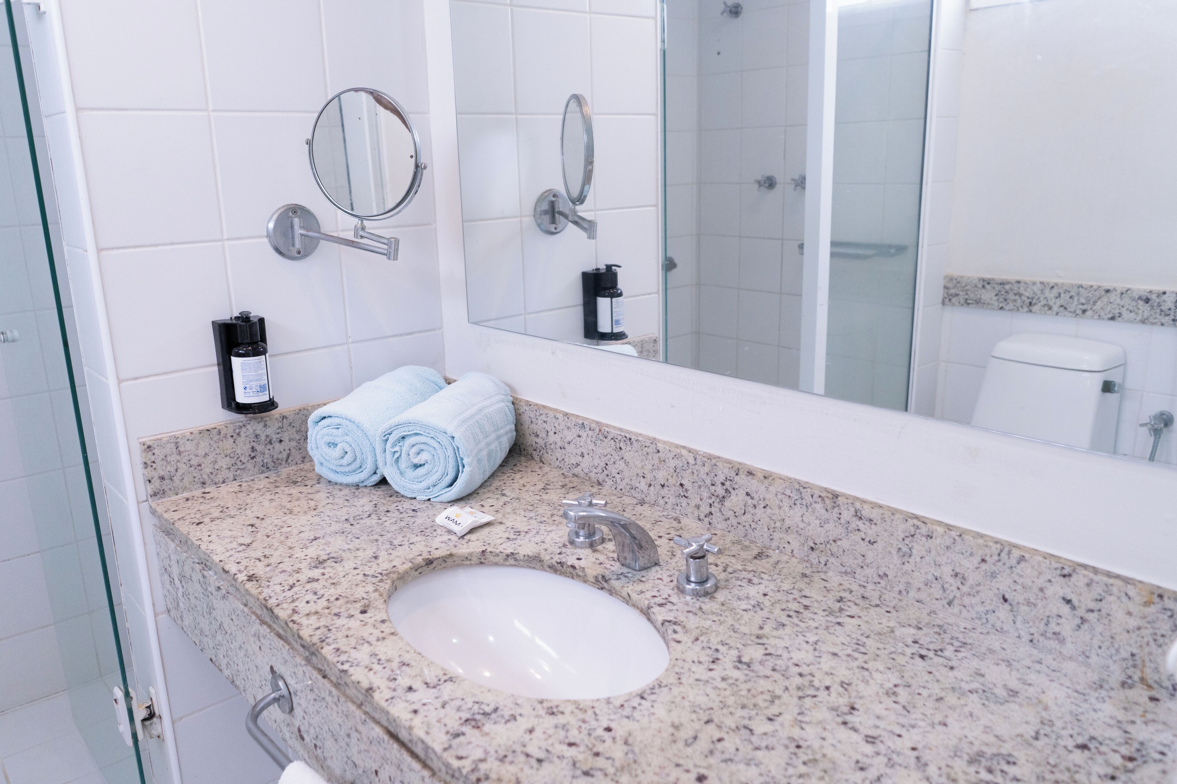 A bathroom with a granite countertop, a sink, two mirrors, and a glass shower enclosure.
