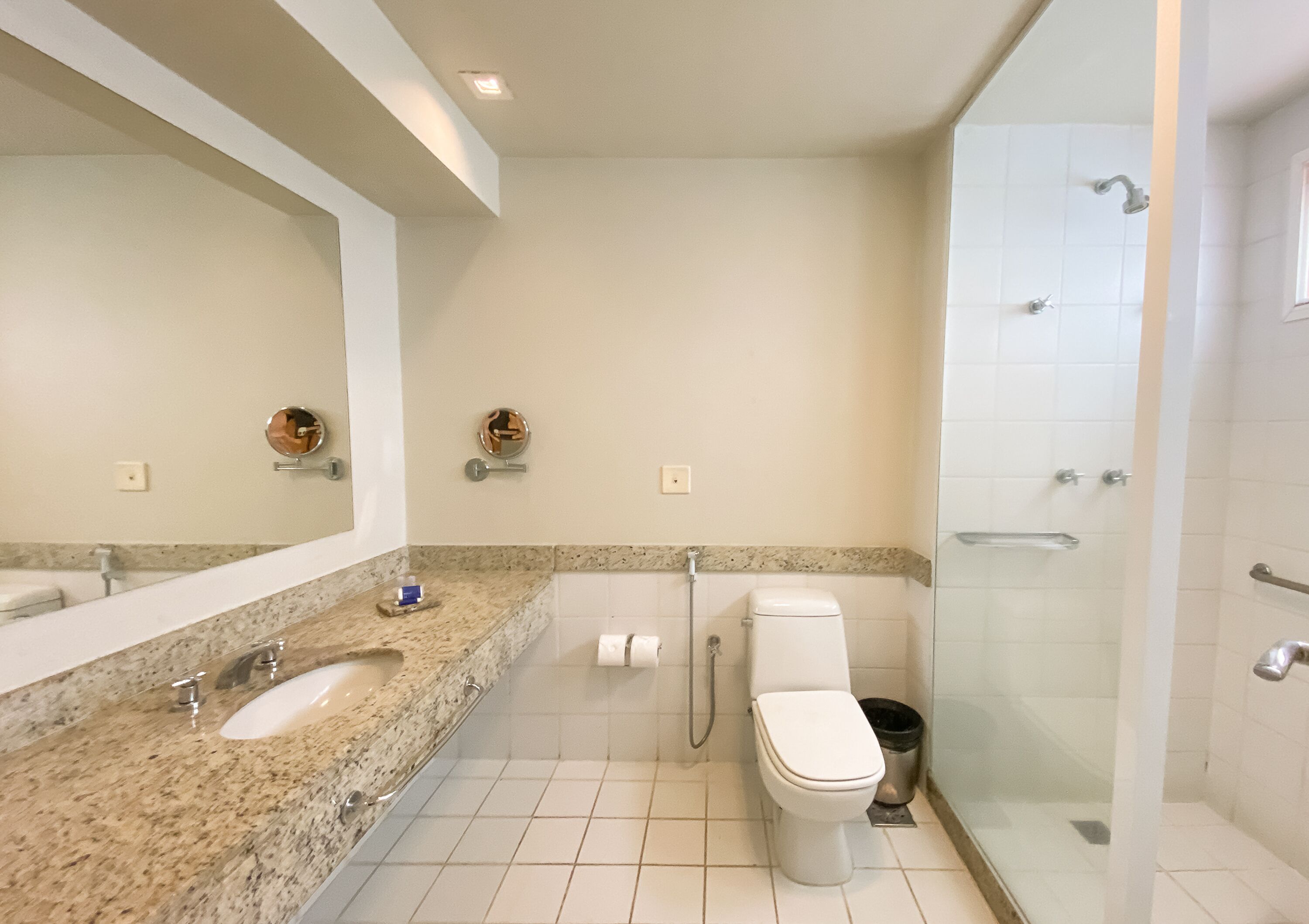 A bathroom with a marble countertop, a toilet, a shower, and a large mirror.