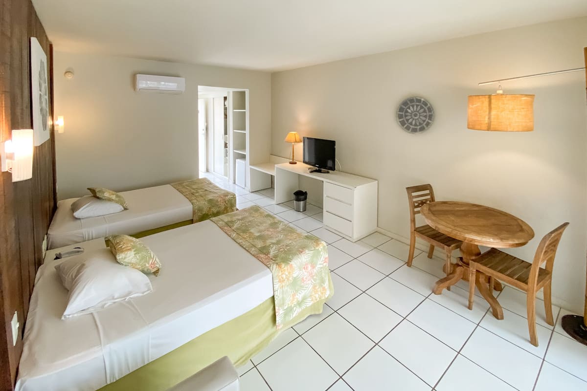 A hotel room with two beds, a desk with a TV, a dining table with chairs, and a small kitchen area.