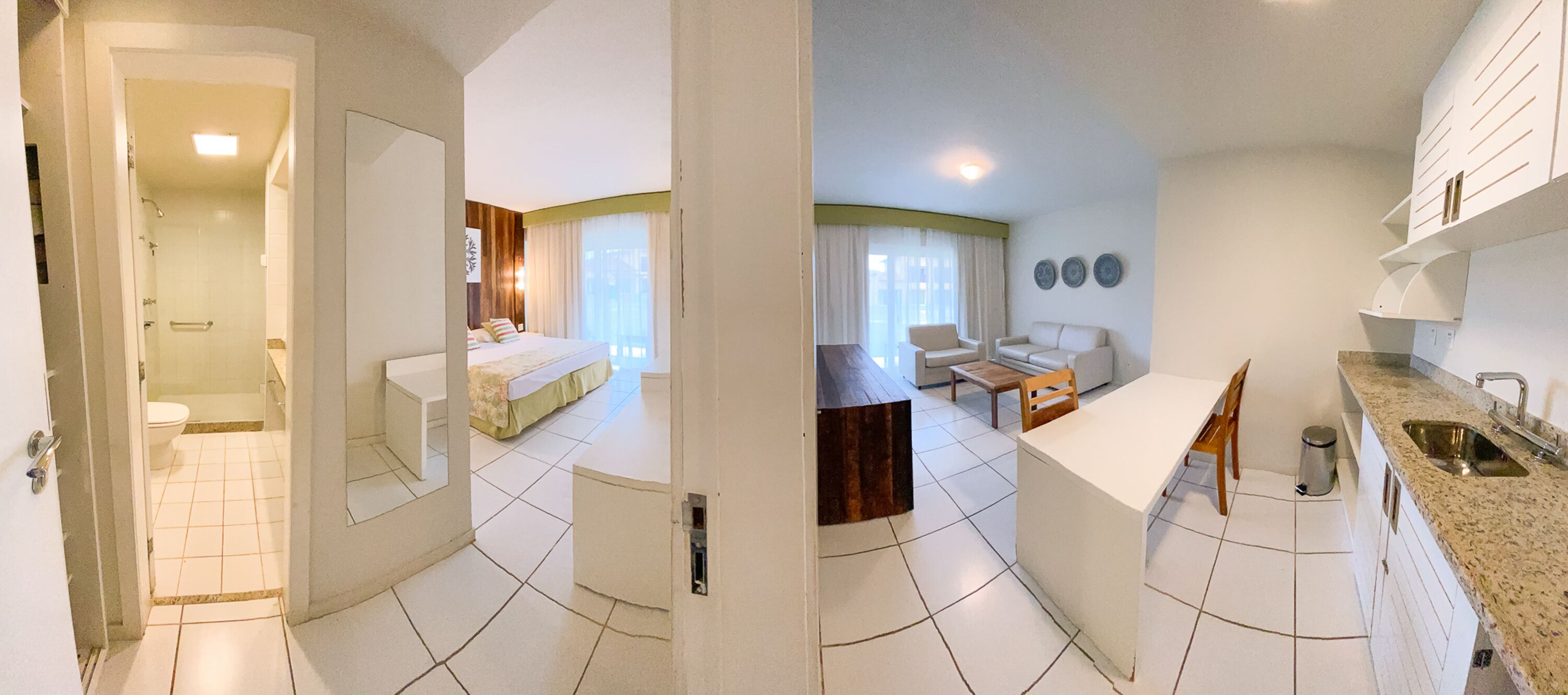 A compact hotel room with a bathroom, a bed, a sofa, a dining area, and a kitchen.