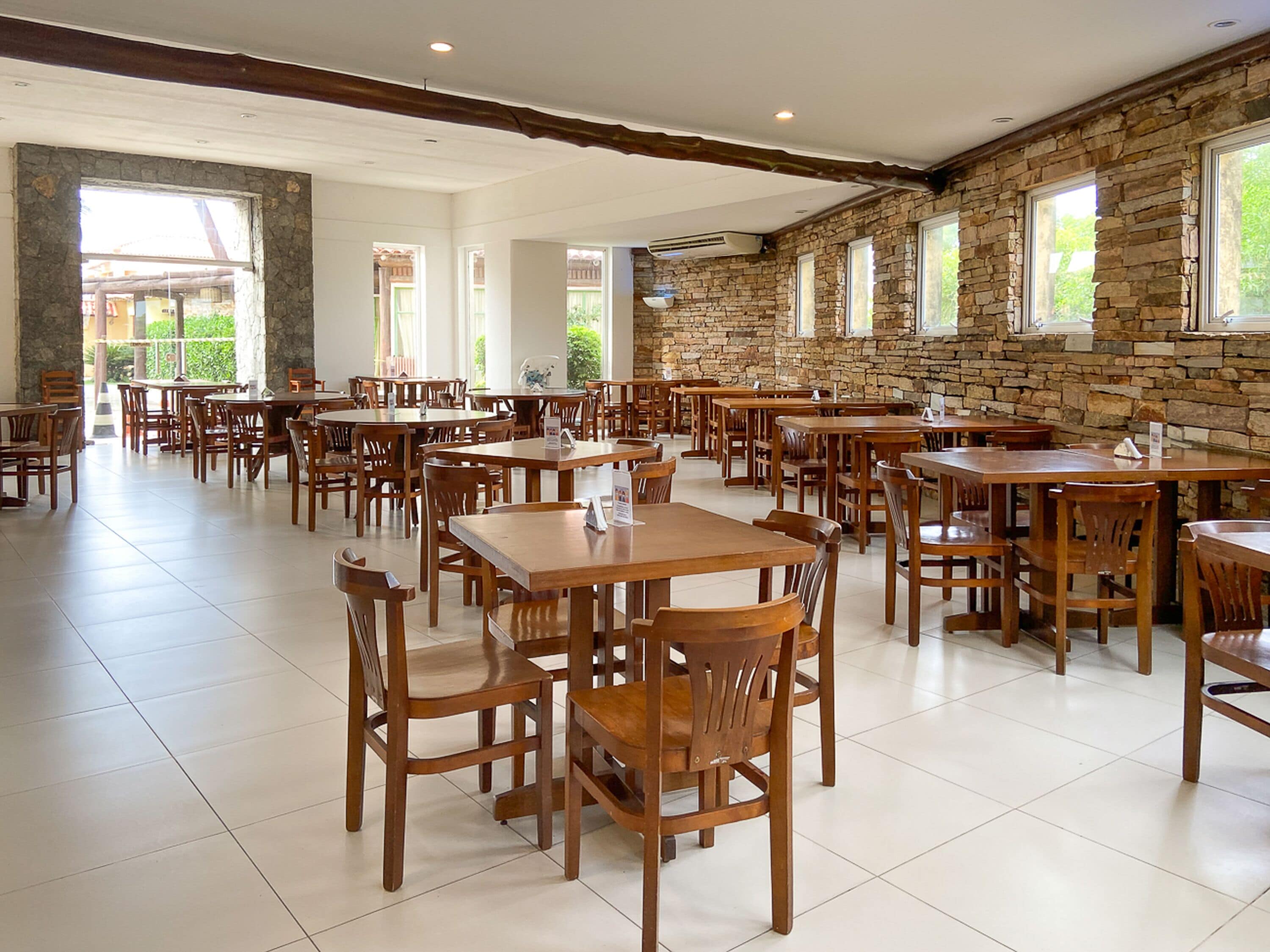 Un comedor amplio con varias mesas y sillas de madera, paredes de piedra y grandes ventanales que dejan entrar luz natural.