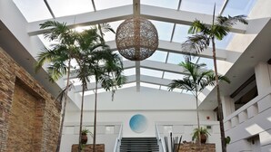 Un atrium moderne avec un plafond de verre, un escalier et des palmiers.