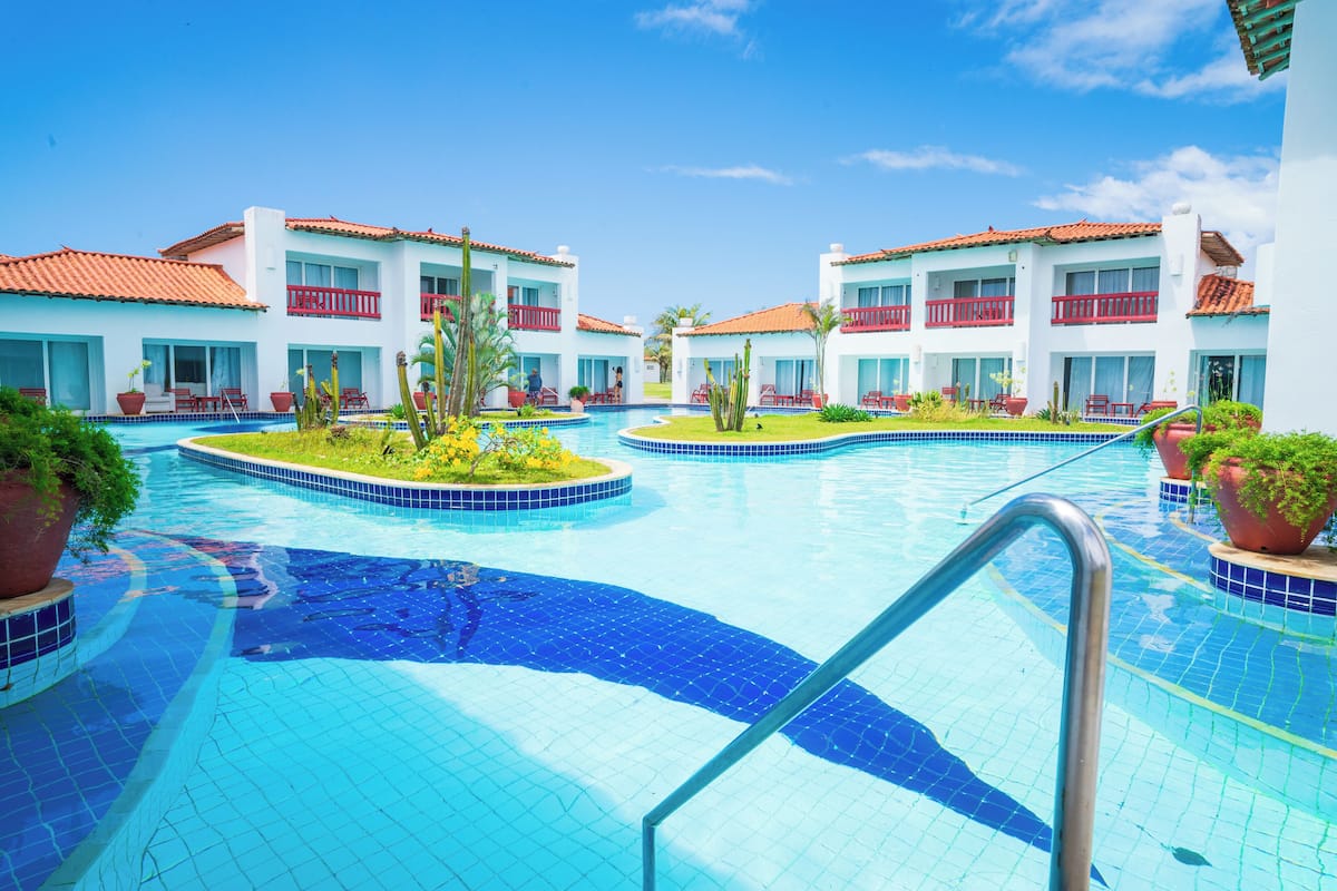 A resort with a swimming pool, multiple balconies, and a clear blue sky.