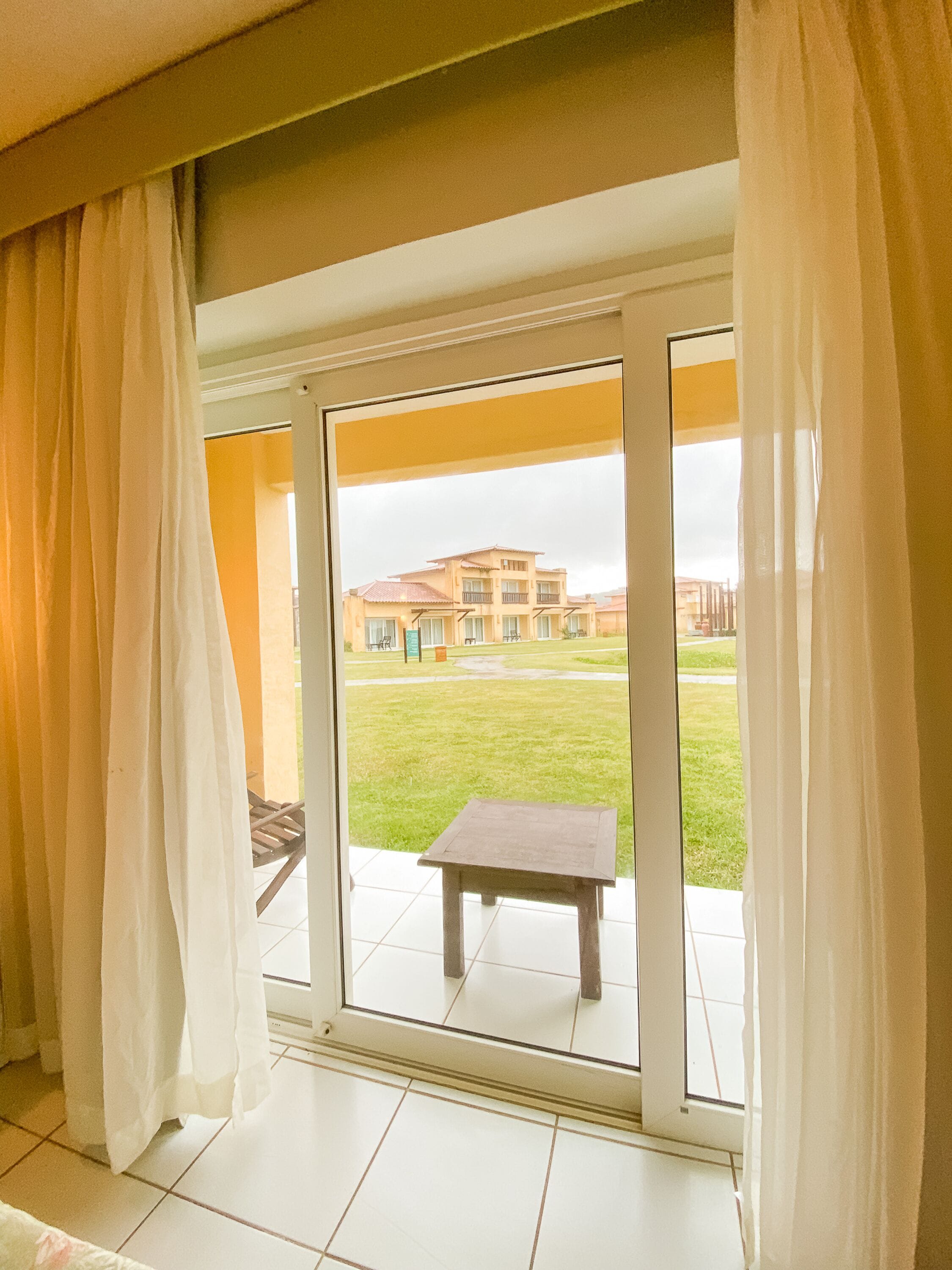Una habitación con puerta corrediza de vidrio que da a un espacio exterior con césped y un edificio al fondo.