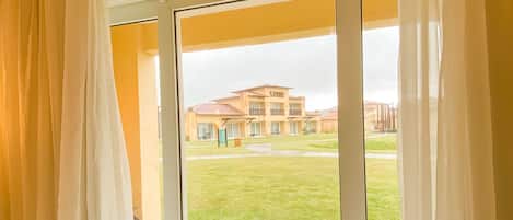 Una habitación con puerta corrediza de vidrio que da a un espacio exterior con césped y un edificio al fondo.