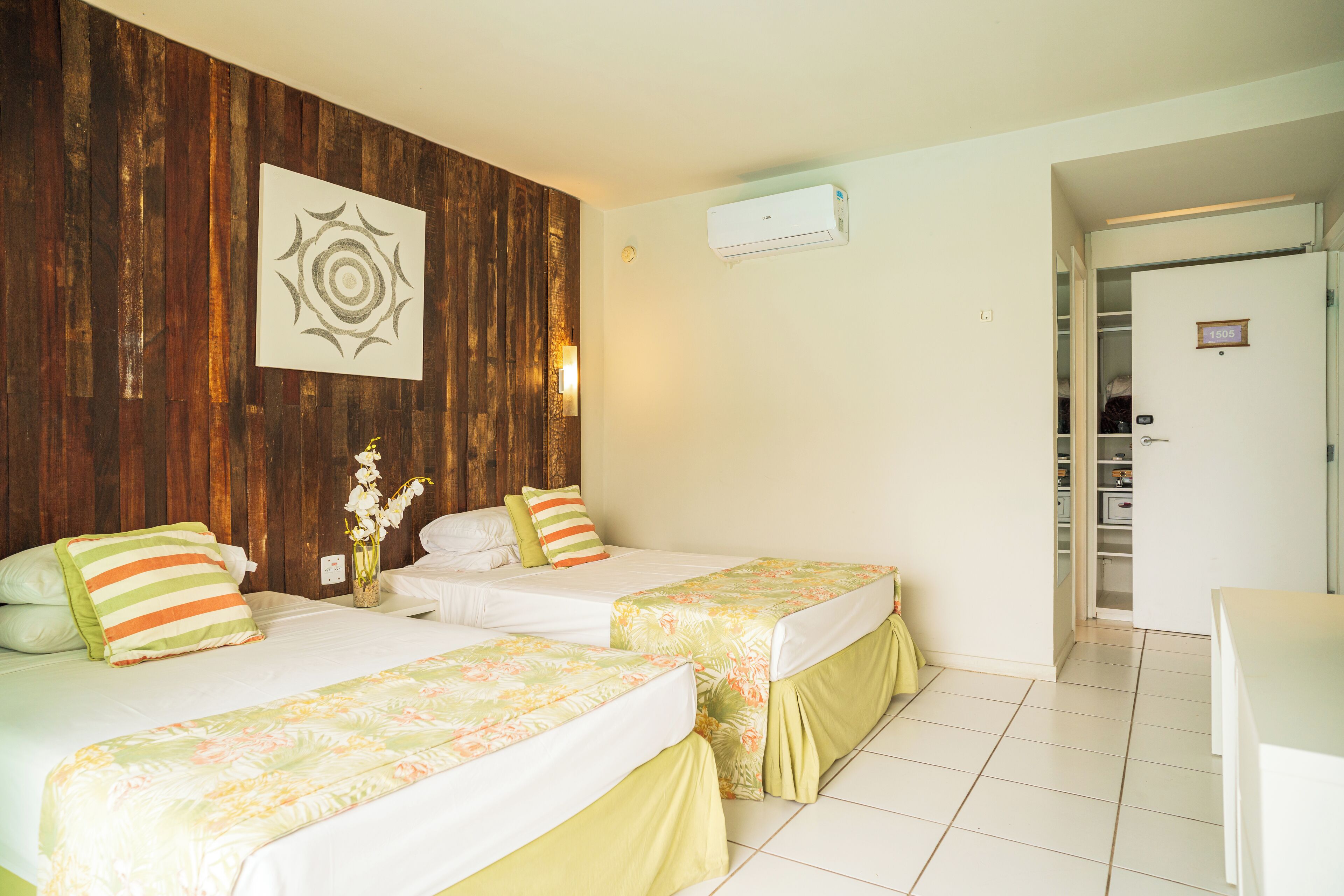 Habitación de hotel con dos camas, un muro decorativo de madera, un aire acondicionado montado en la pared y una puerta que da a un armario.