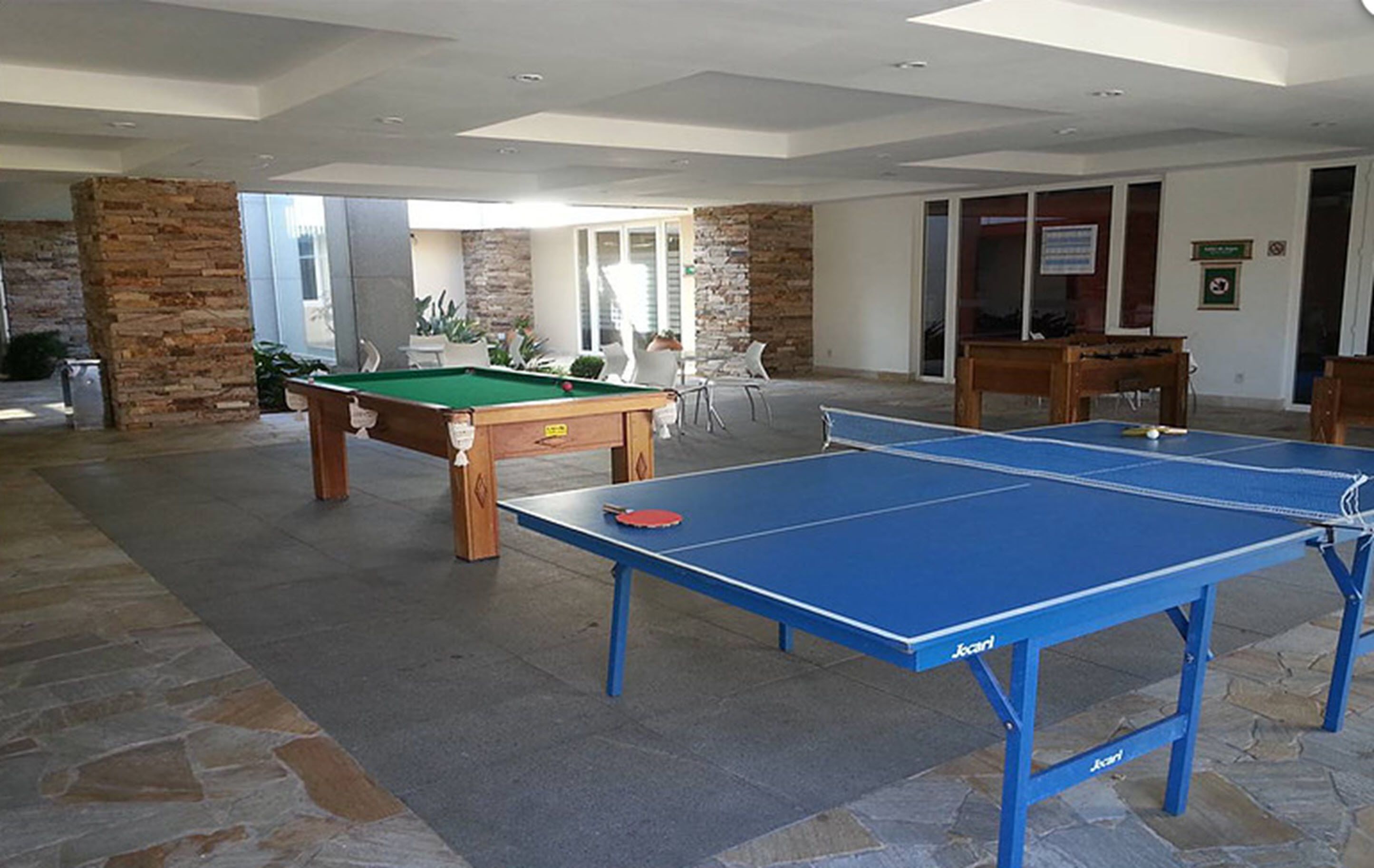 Un tavolo da biliardo e un tavolo da ping pong in un'ampia area interna con pavimento e parete in pietra.